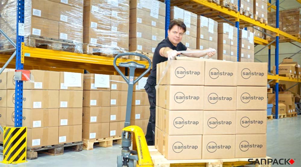 Mitarbeiter sichert Kartons auf Palette mit sanstrap® Dehnband im Lager
